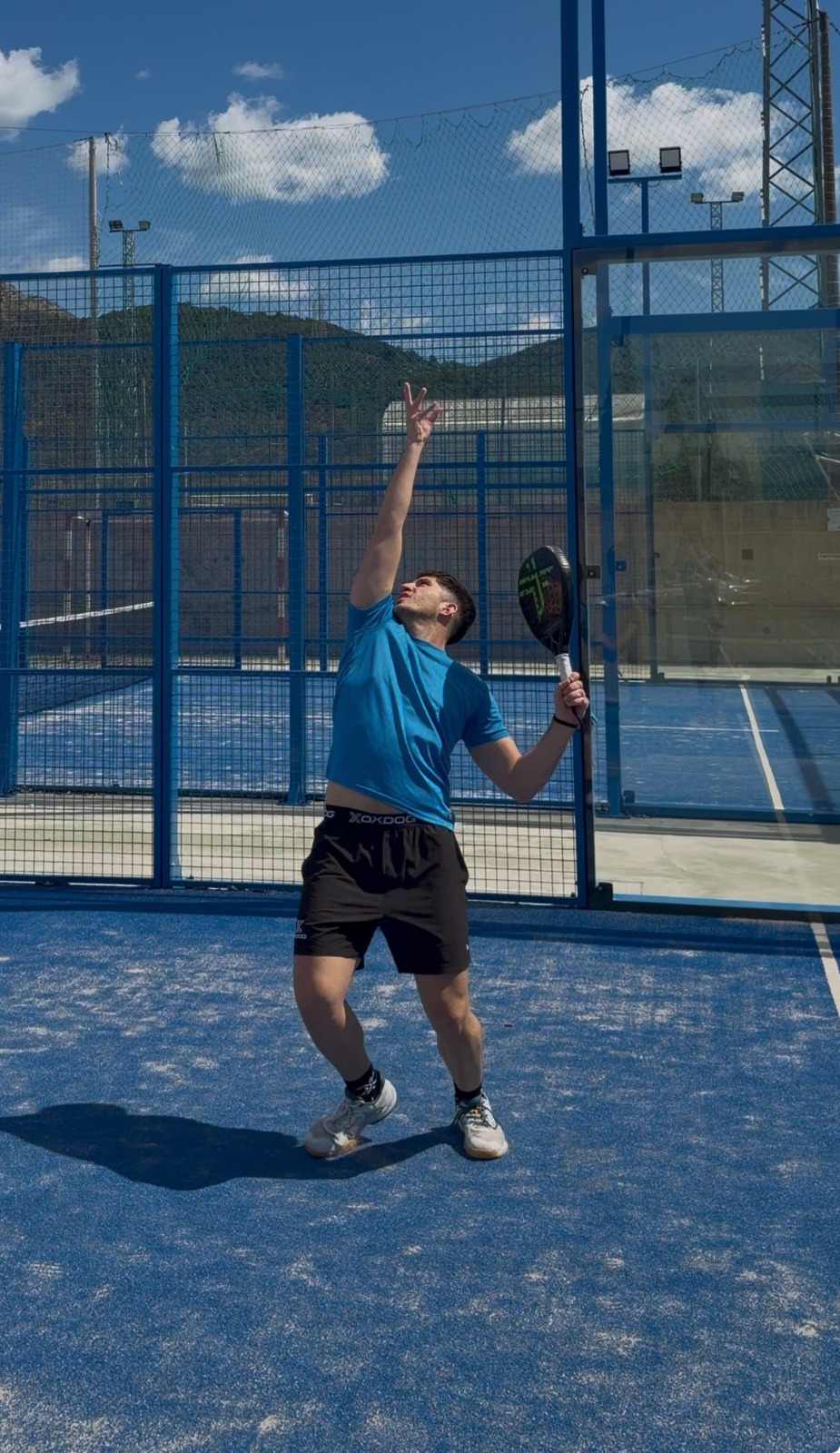 Sorin, coach at La Casa De Padel, preparing to serve during a training session on an outdoor blue padel court.